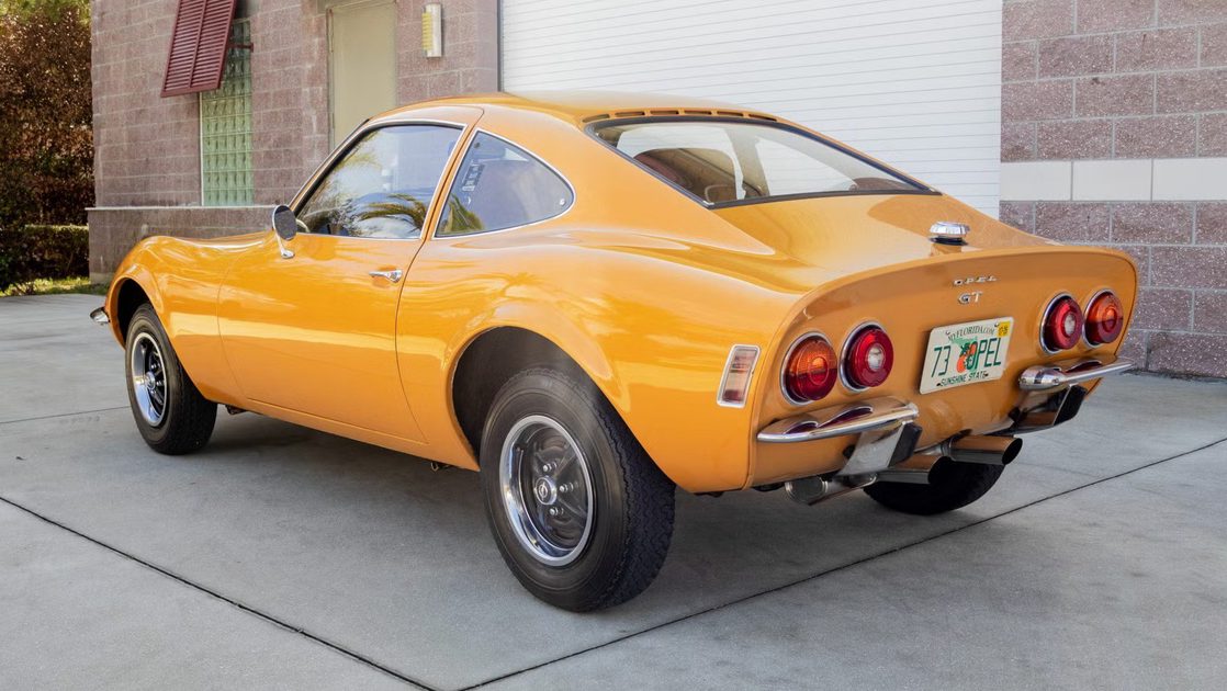 rear three quarter view of yellow coupe parked on driveway with round taillights.