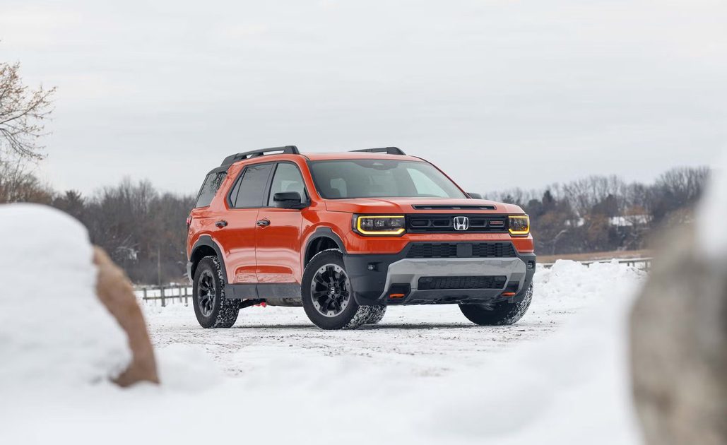front three quarter view of orange suv parked on snow covered ground with headlights on.