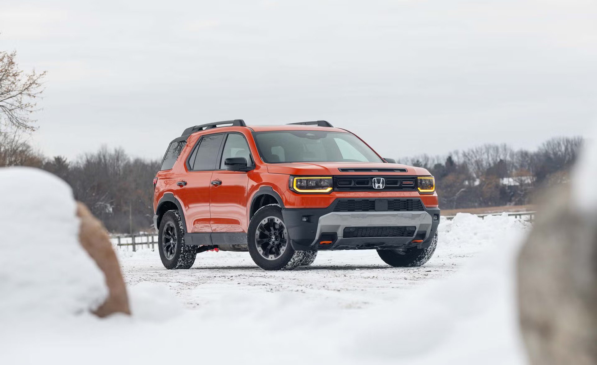 front three quarter view of orange suv parked on snow covered ground with headlights on.